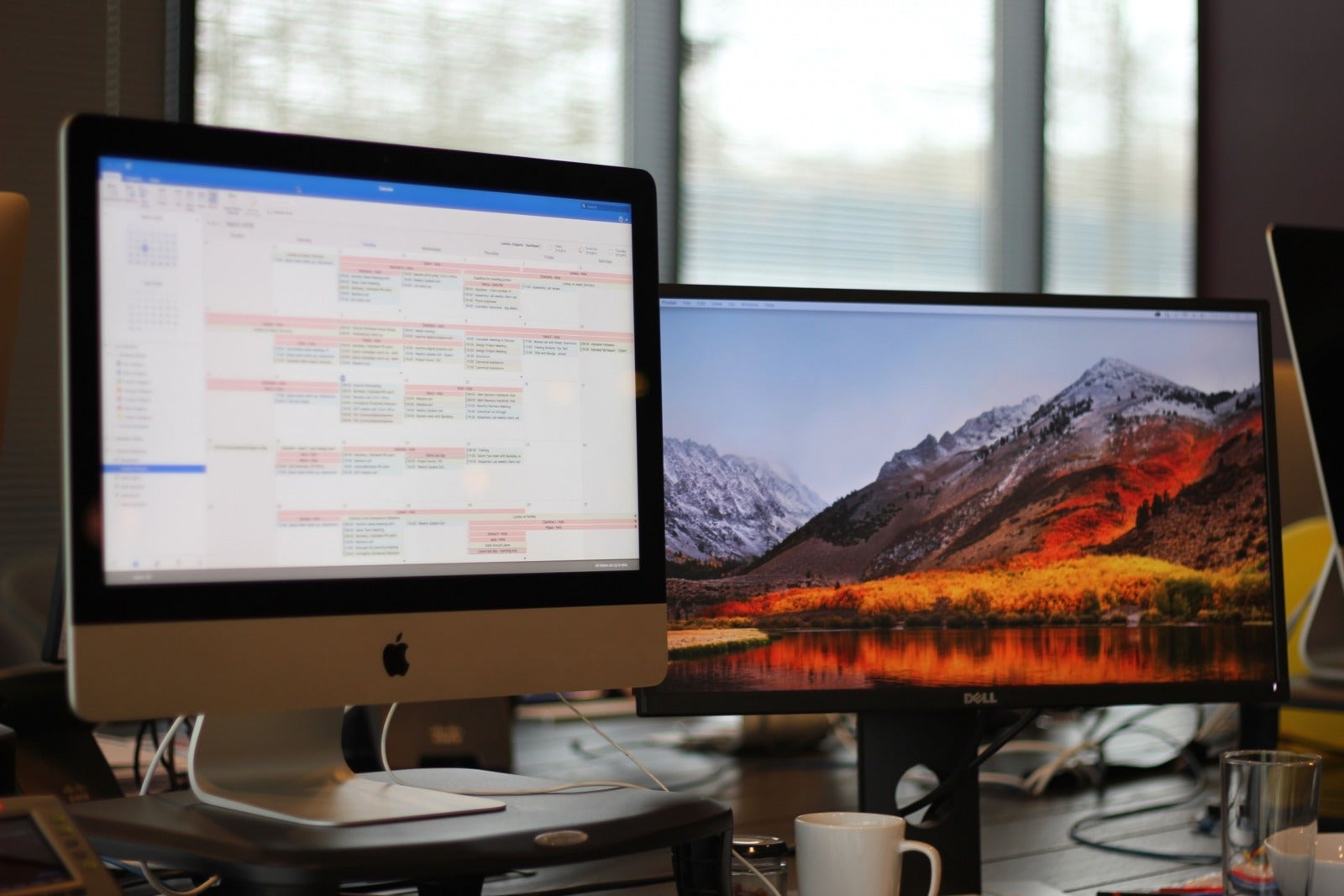 A desk with two computer monitors, one showing a calendar. 