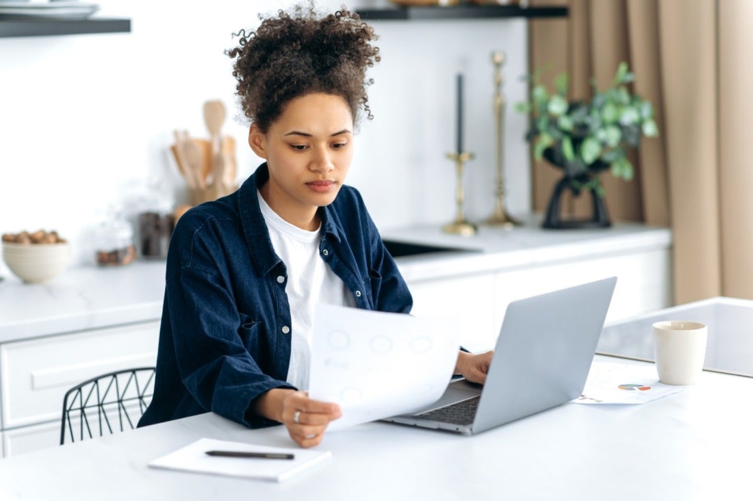 Young Adult African American Woman Reading a Paper Near a Laptop