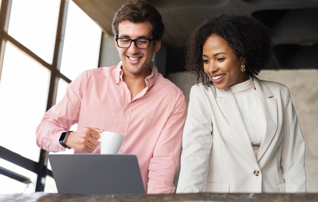 Two business professionals smiling, drinking coffee, and looking at computer in an office