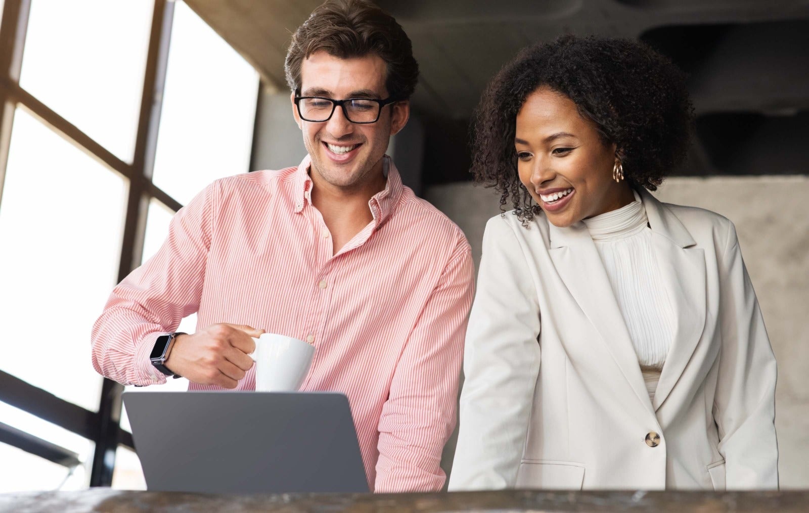 pair of colleagues stand at desk looking at laptop