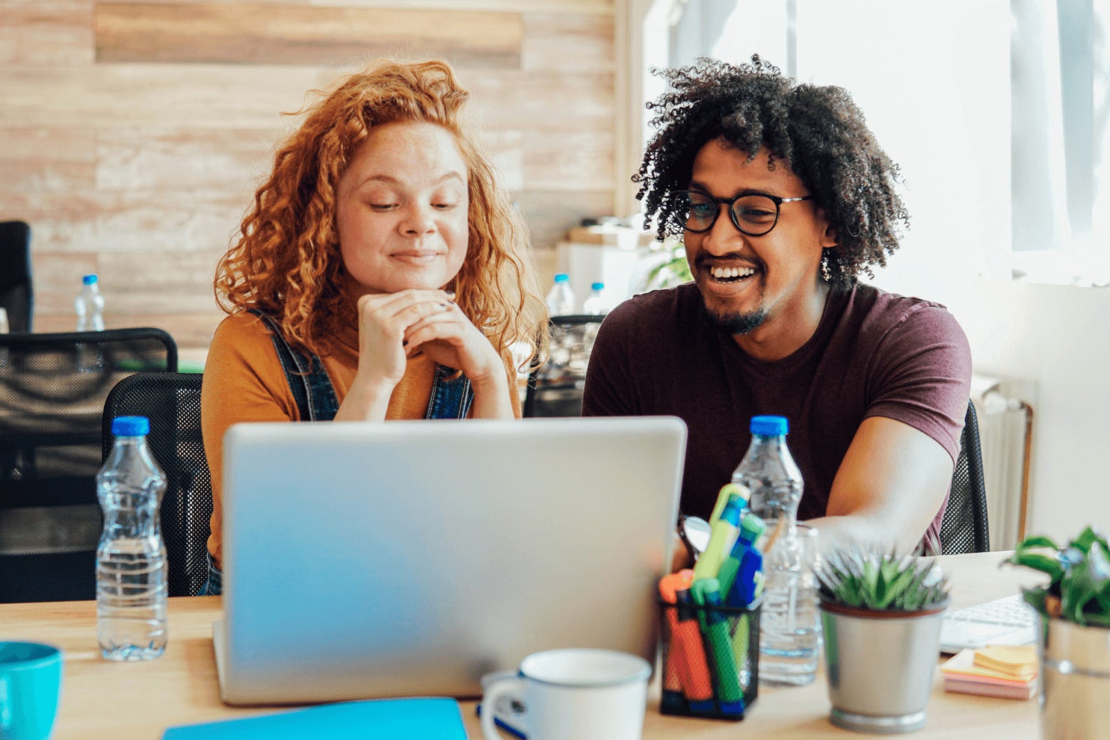 two colleagues smile while looking at laptop on work desk
