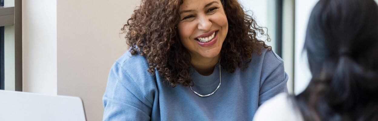 An interviewer smiles at a job candidate while taking notes during their conversation.